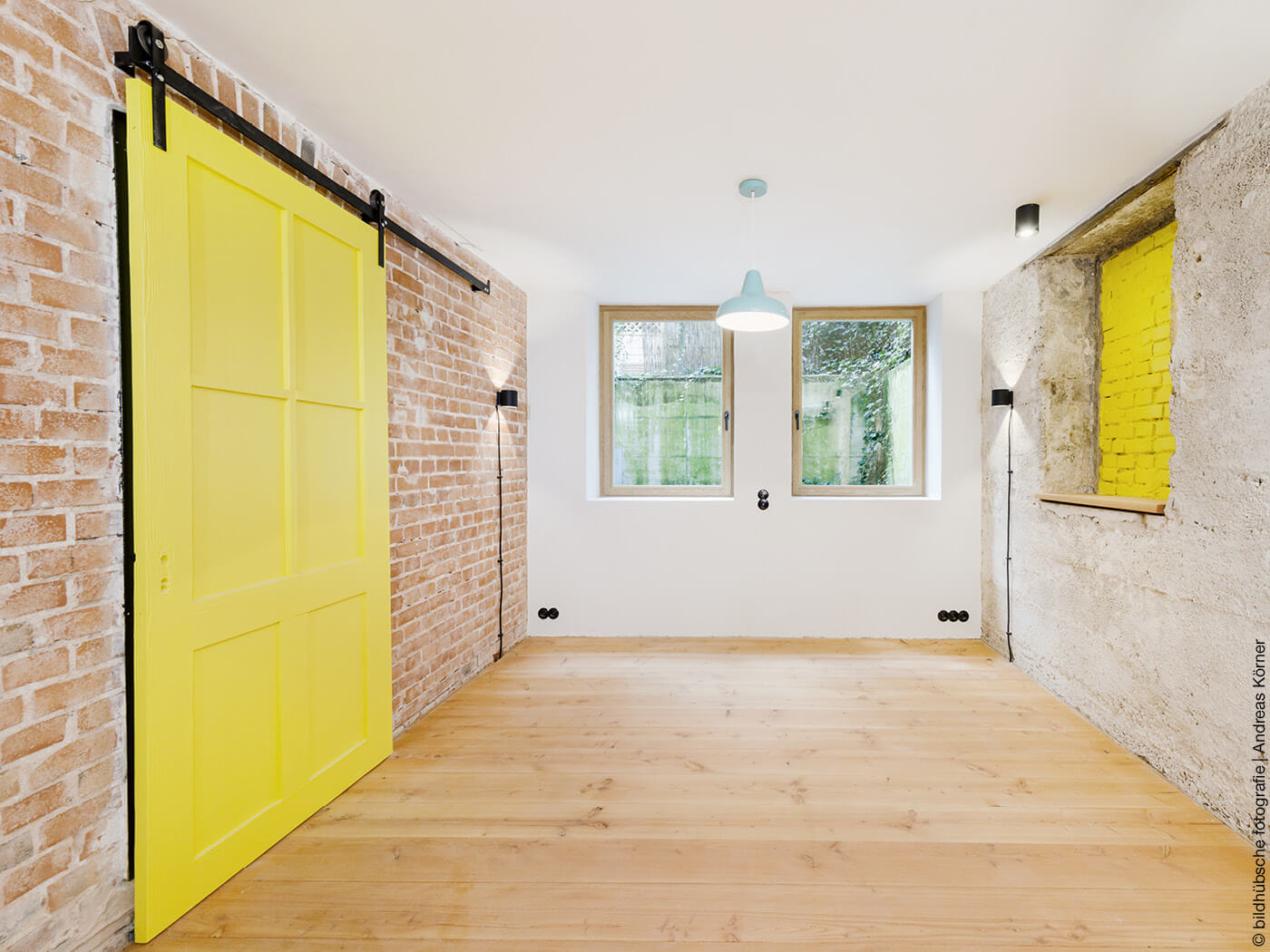 Raum mit Holzdielen, unverputzte Wänden und gelber Schiebetür