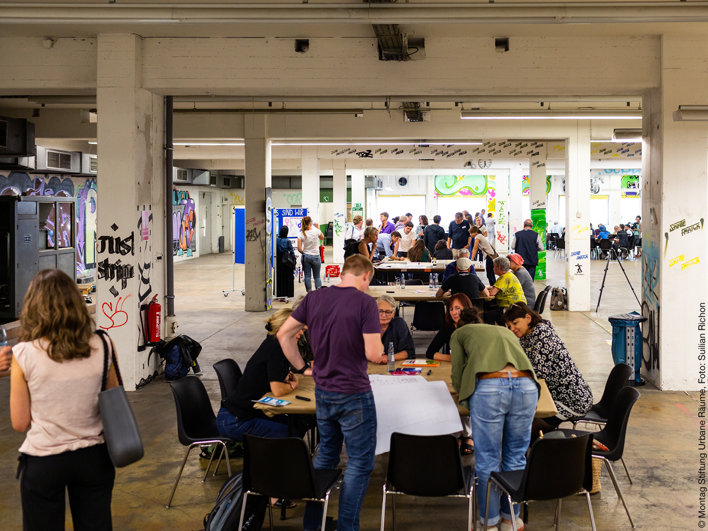 Menschen diskutieren an Tischen in Industriehalle