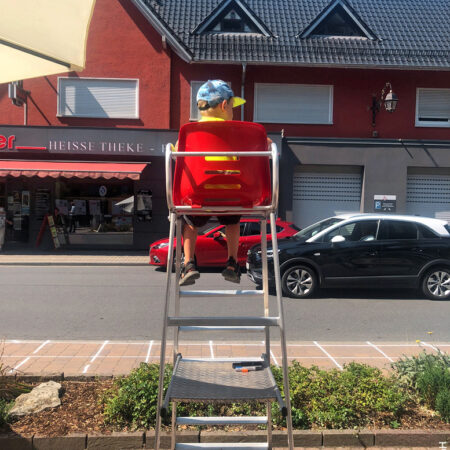 Kind sitzt am Straßenrand auf einem Hochsitz