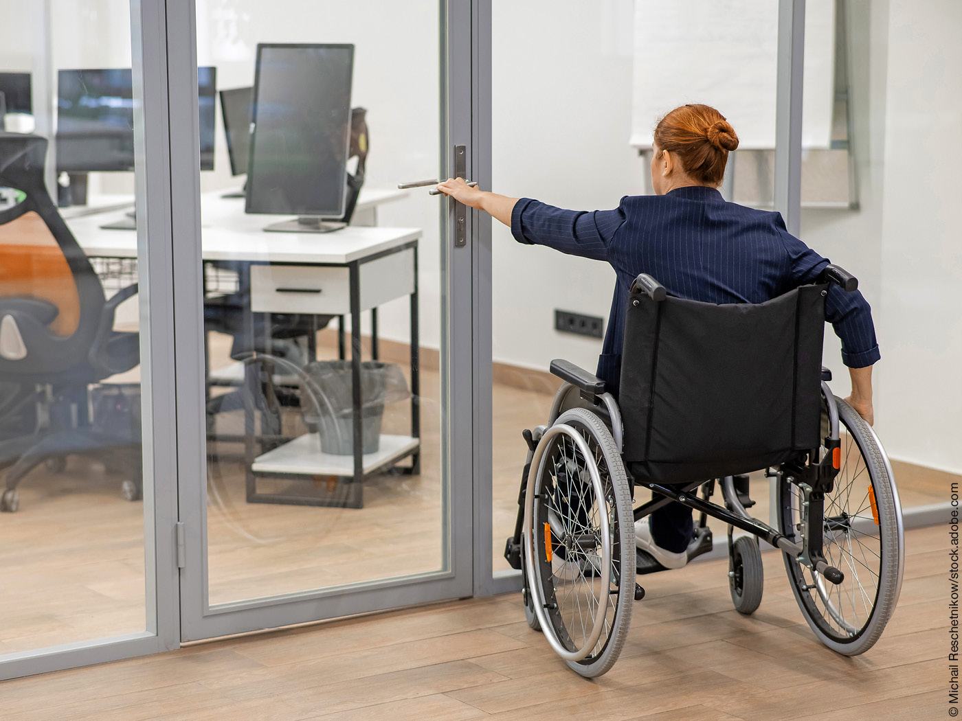 Frau im Rollstuhl versucht, eine verschlossene Glastür zu öffnen.
