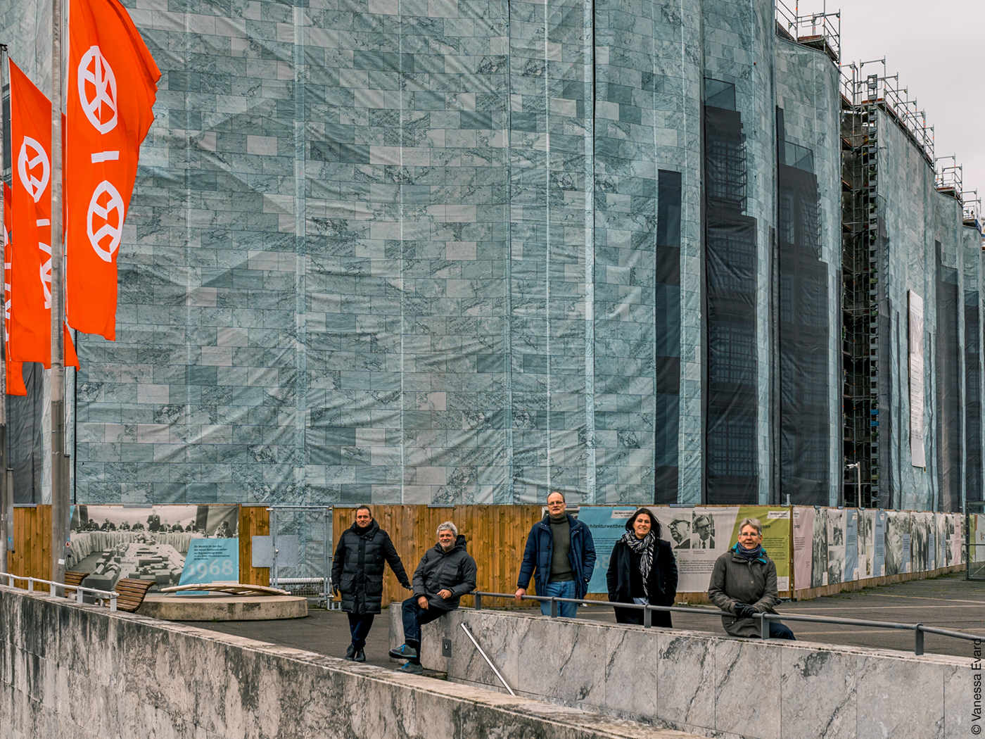 Eingepackte Hausfassade mit Bauzäunen, davor Menschen