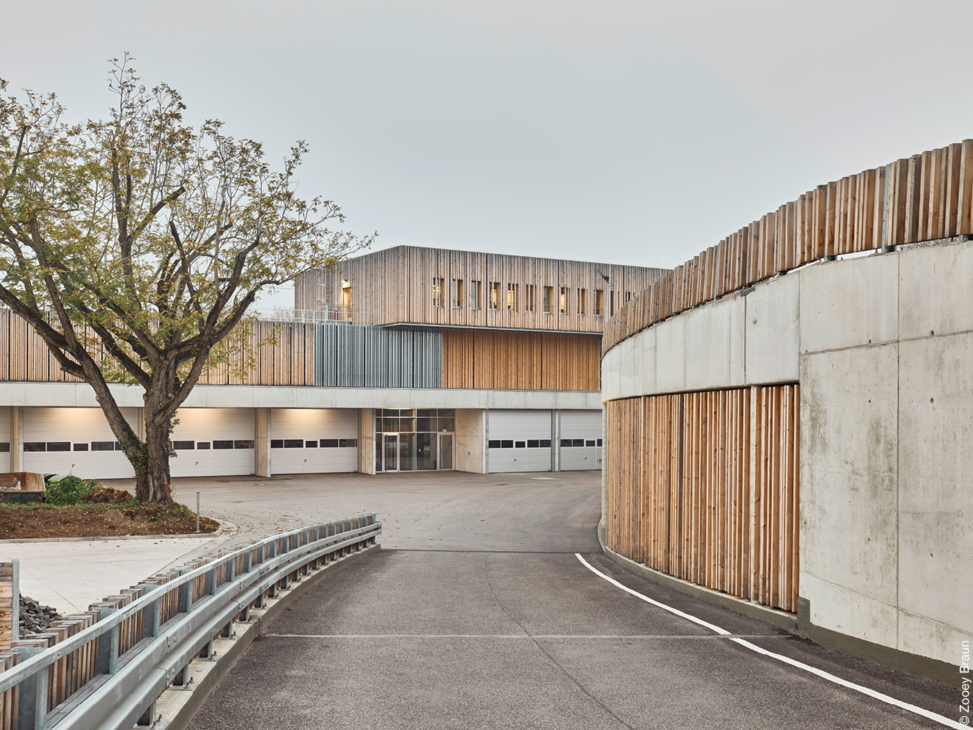 Menschenleer Auffahrt zu einem Betriebshof mit beigebraun-roströtlicher Fassade.