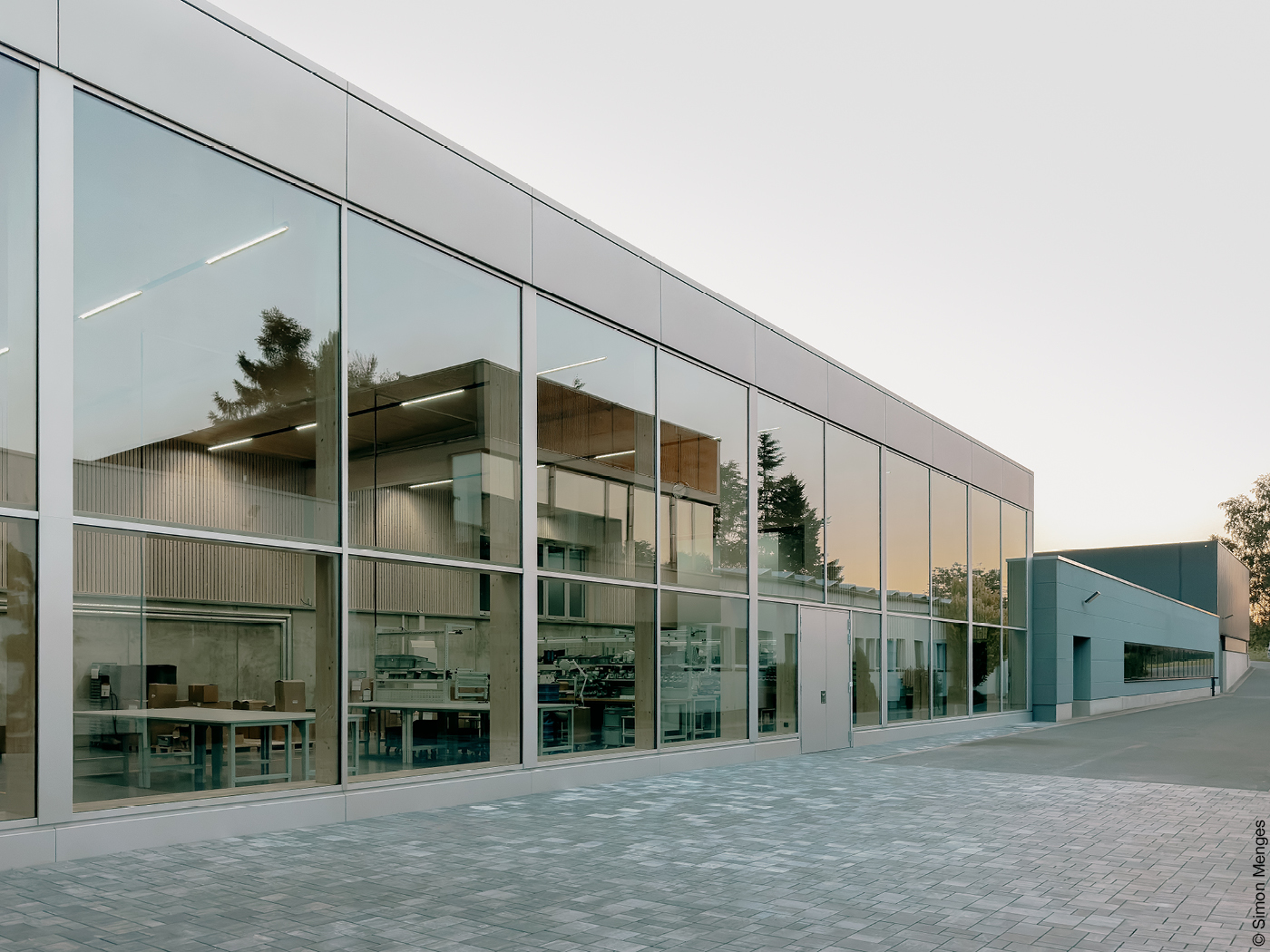 Glasfront der Werkshalle einer Fabrik, in deren Fenstern sich die untergehende Sonne spiegelt.