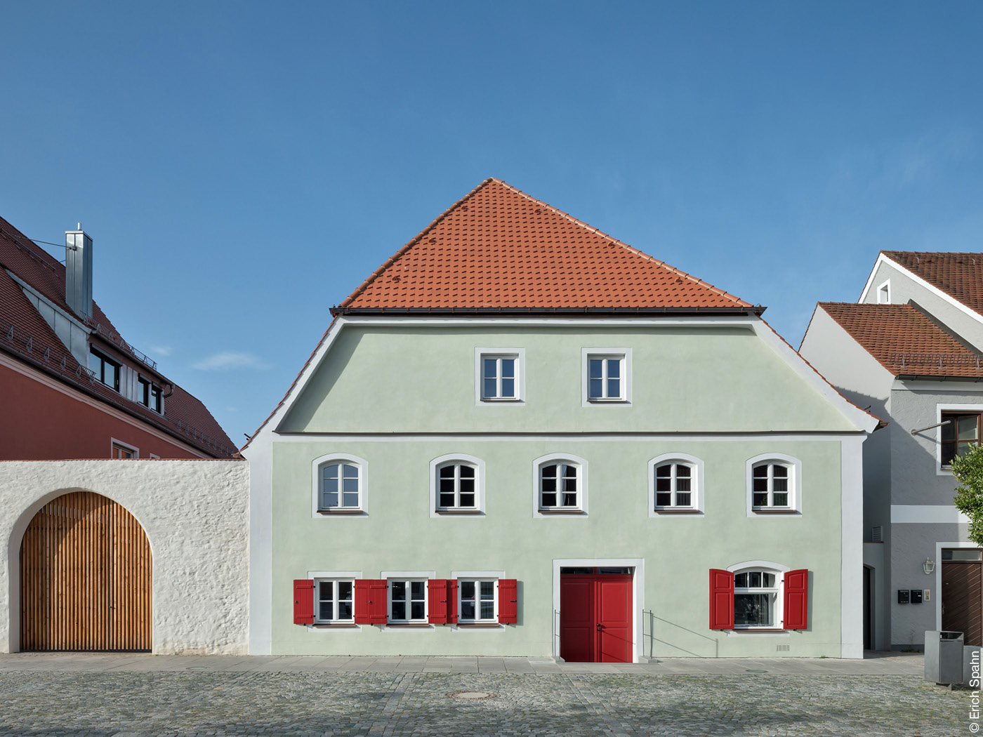 Haus mit lindgrüner Fassade und roten Fensterläden.