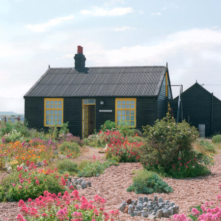 Schwarze Holzhütte in Garten mit Kiesflächen und bunten Blumen