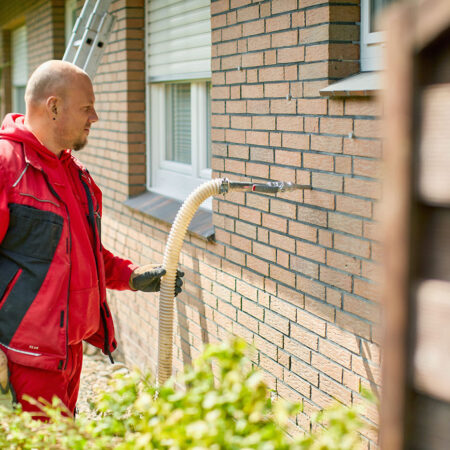 Mann füllt Einblasdämmung durch Schlauch in Hauswand ein