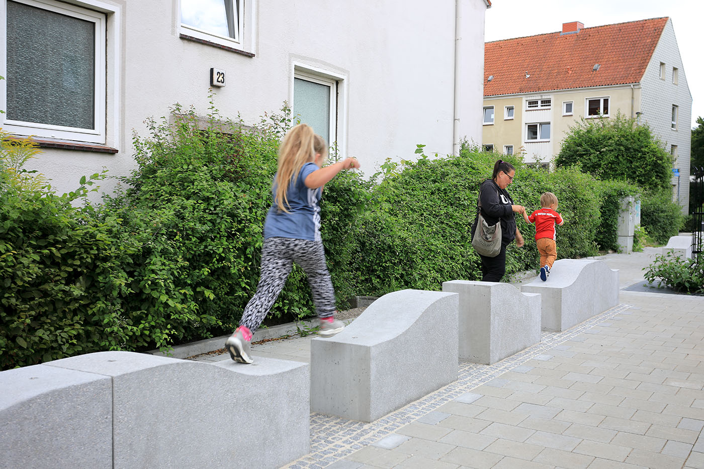 Kinder springen auf Steinquadern neben dem Bürgersteig