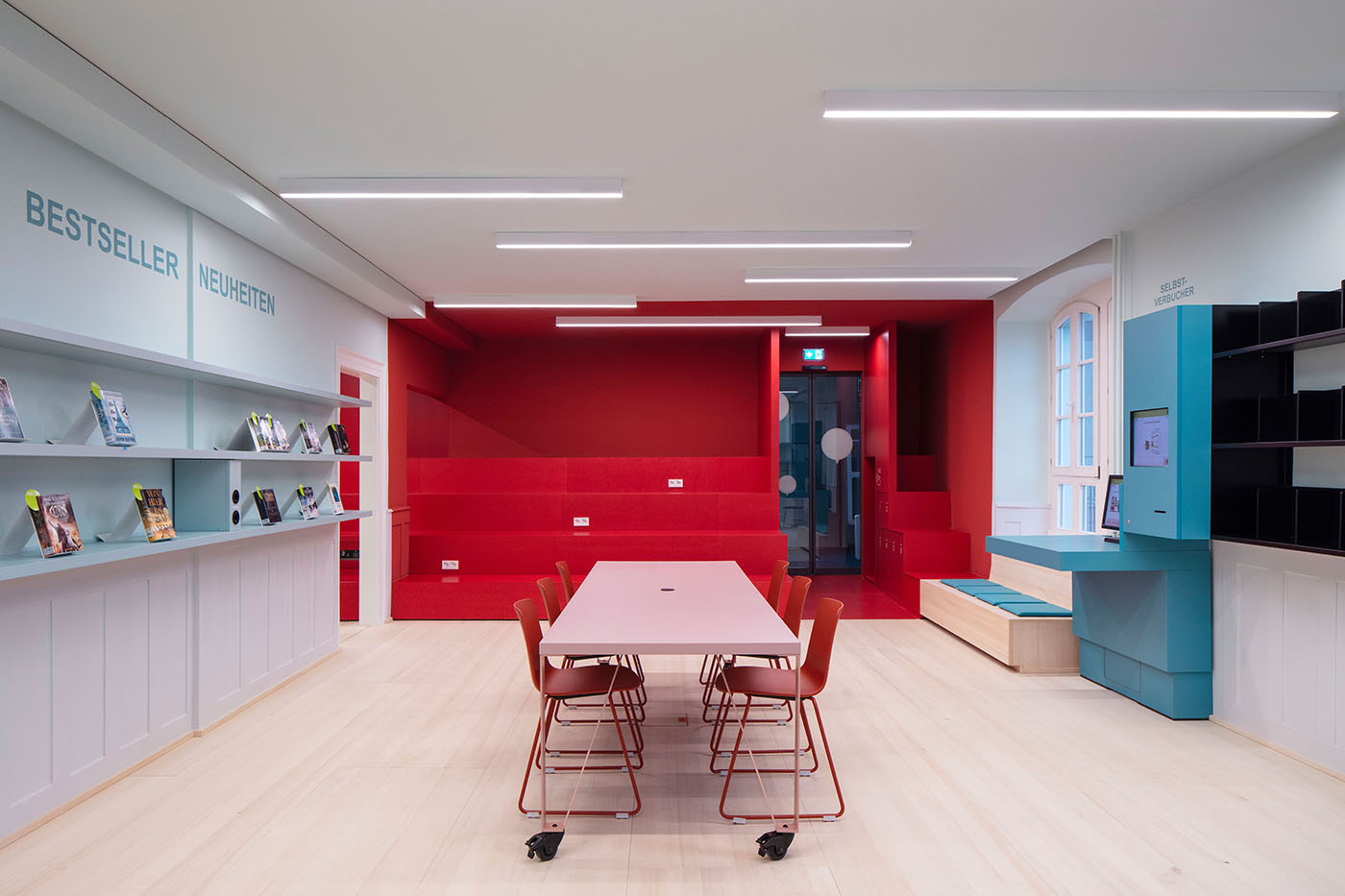 Innenraum Bibliothek von Waldshut mit roten und blauen Treppen, Bücherregalen und einem rosa Tisch mit roten Stühlen