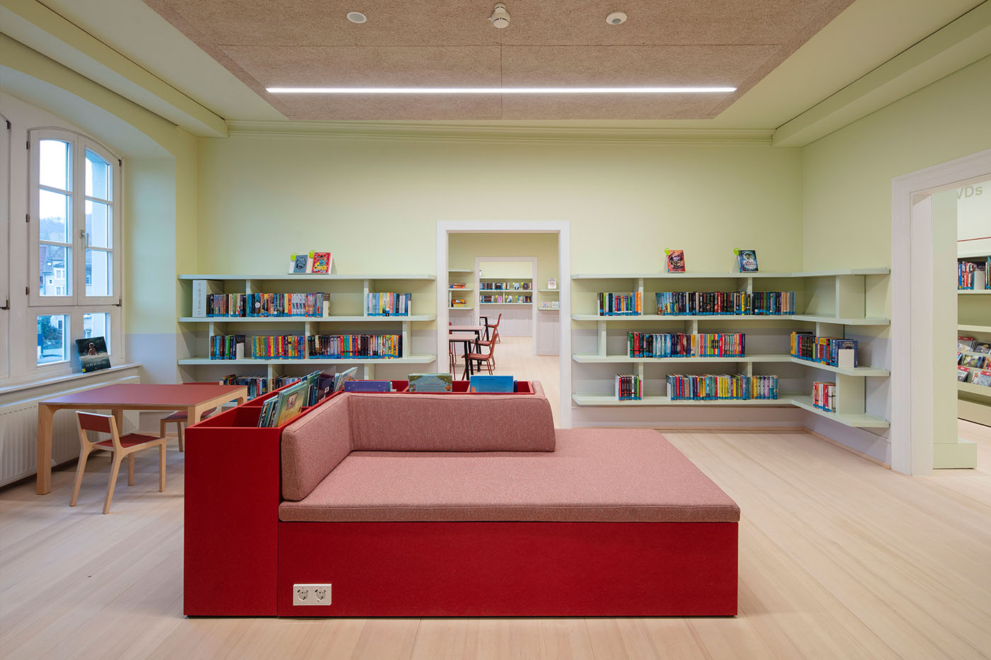 Innenraum der Bibliothek in Waldshut mit einer großen Sitz- und Liegefläche in Rosa und Rot und Bücherregalen an den Wänden.