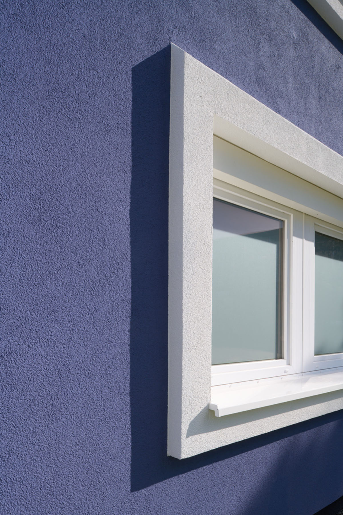 Lilafarbene Hauswand mit einem Fenster mit weißem Fensterrahmen.