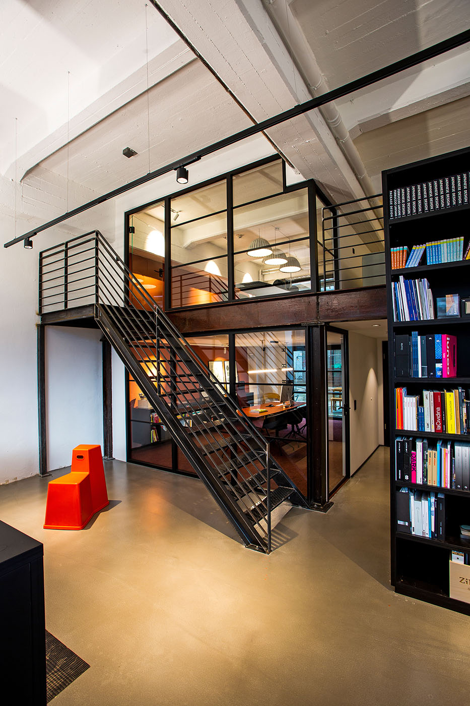 Hoher Raum innerhalb einer Fabrik mit schwarzer Treppe und einem gläsernen Büro.