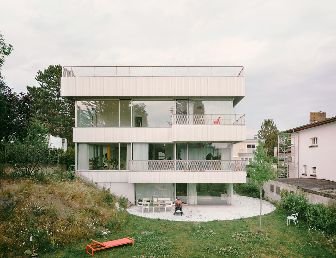 Quadratisches Haus mit breiten Fensterfronten, Balkonen und einer kreisförmigen Terrasse und Garten im Erdgeschoss