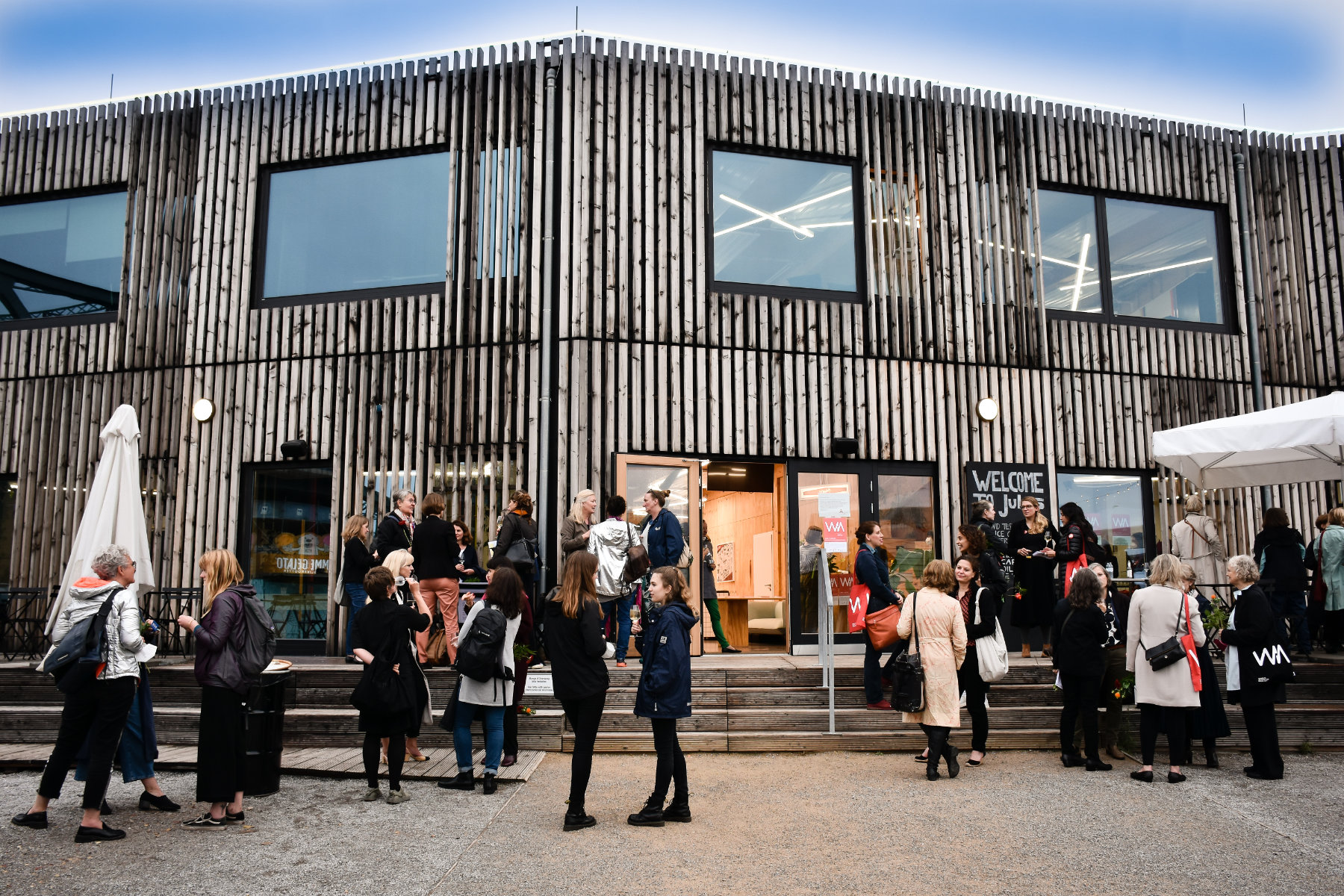 Frauen auf dem WIA Festival vor einem Gebäude mit Holzfassade und unterhalten sich