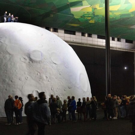 Künstlich installierter Mond in einer dunklen Kunsthalle mit vielen Besuchern