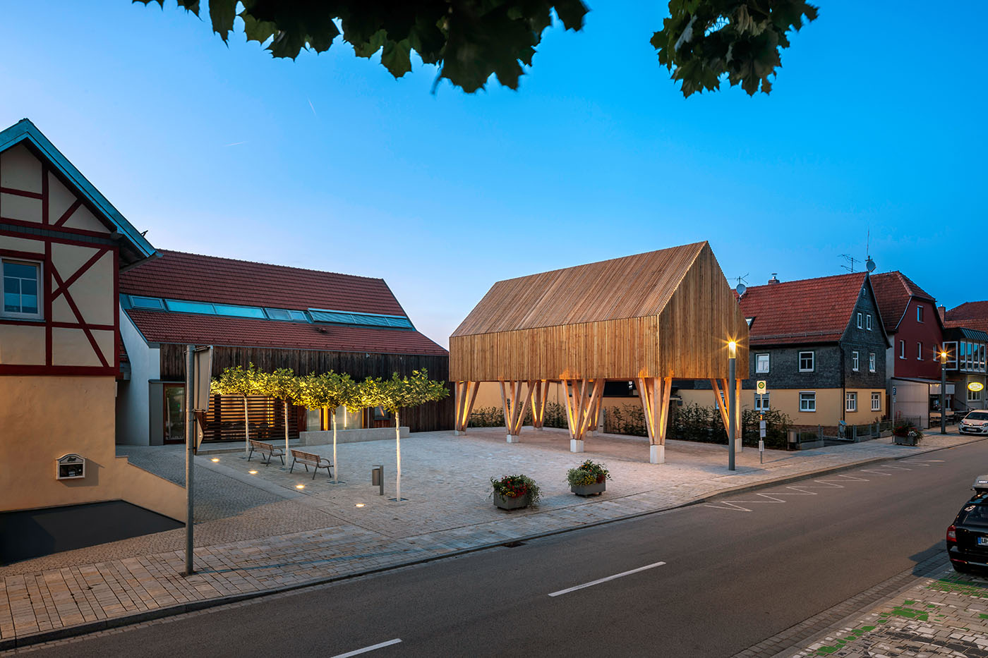 Platz mit Bänken, offene Halle mit hohem Holzdach und Bushaltestelle